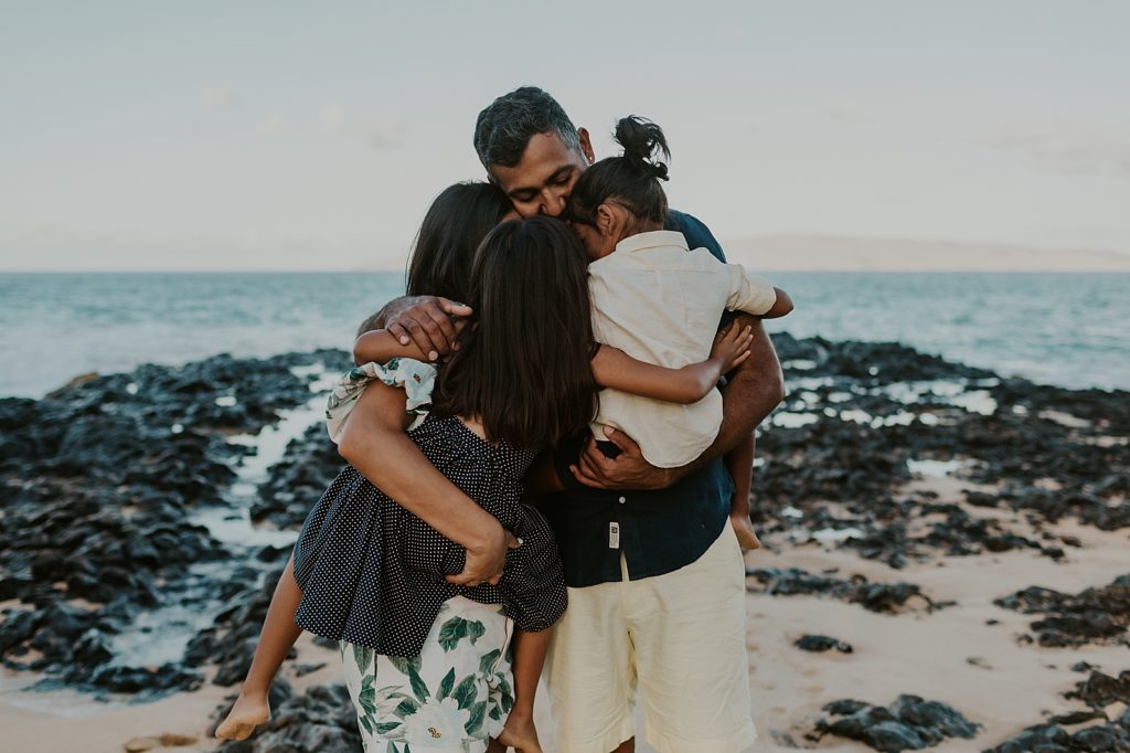 Family hugging on the beach by volcanic rock