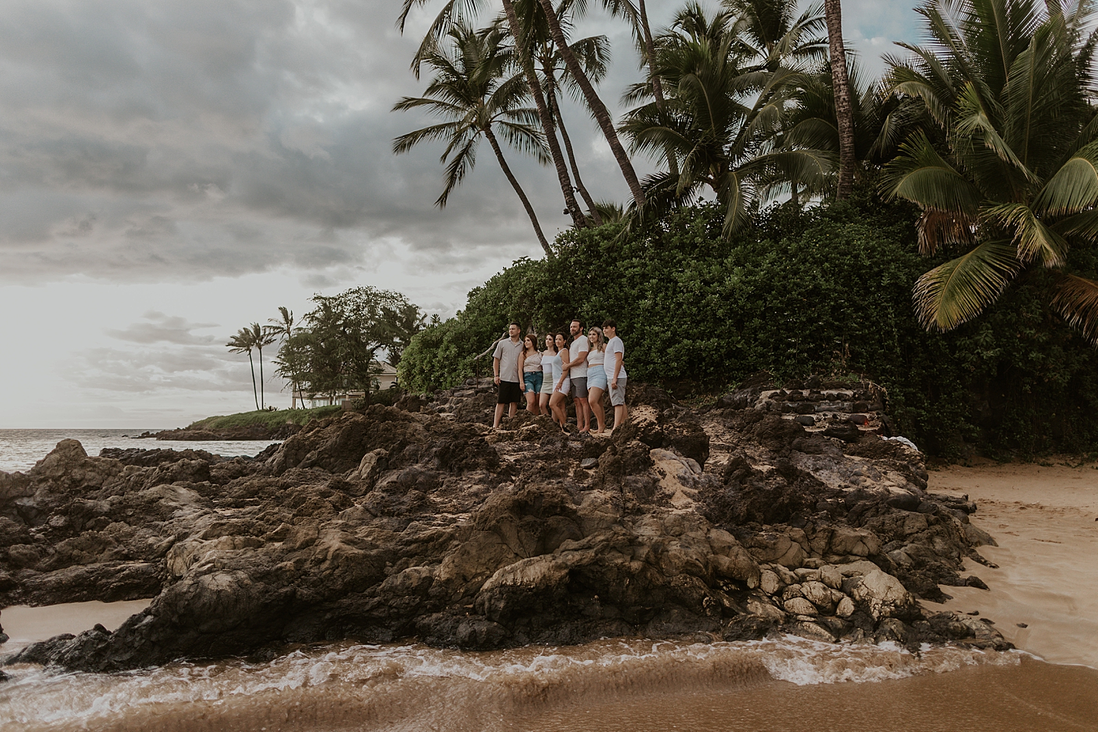 Family standing on drift beach rock withn palm trees