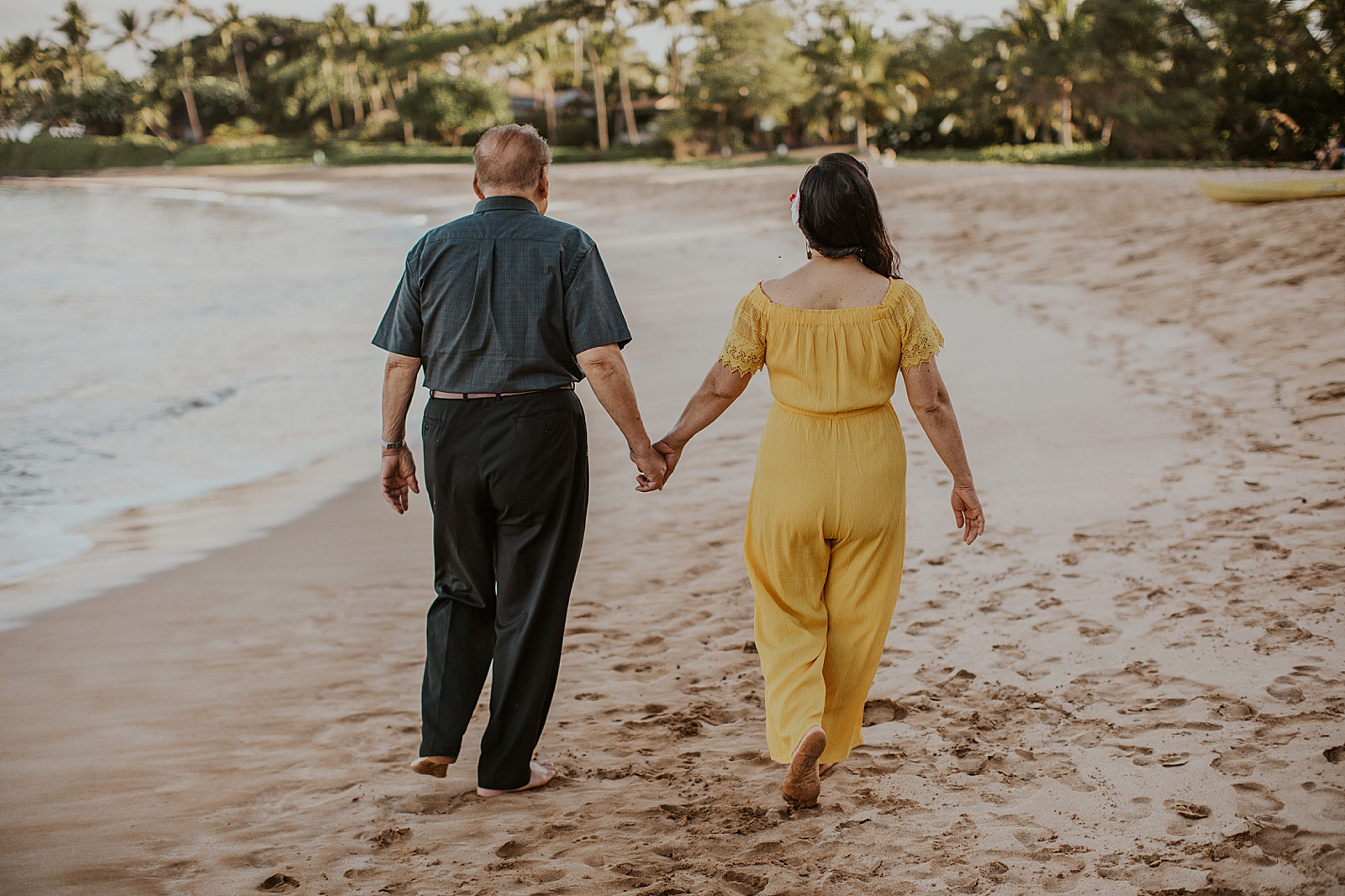 Grandparents holding hands and walking on sand together