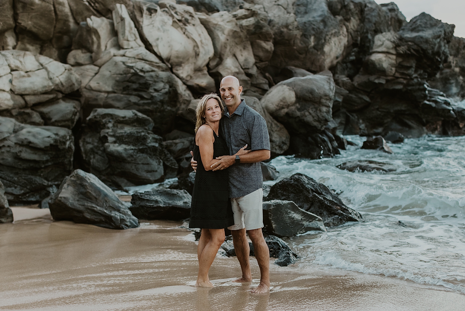 Couple holding each other in front of rock cliff on the beach