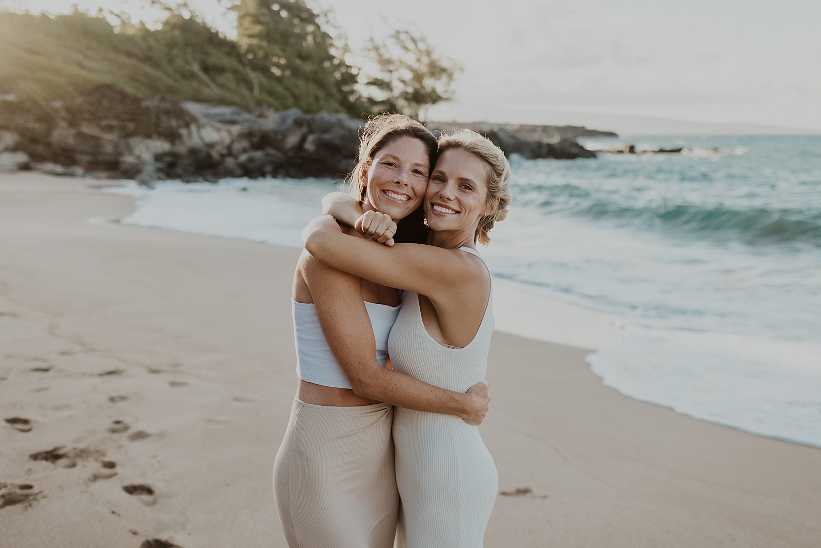 Sisters hugging each other and standing on the sand by the ocean