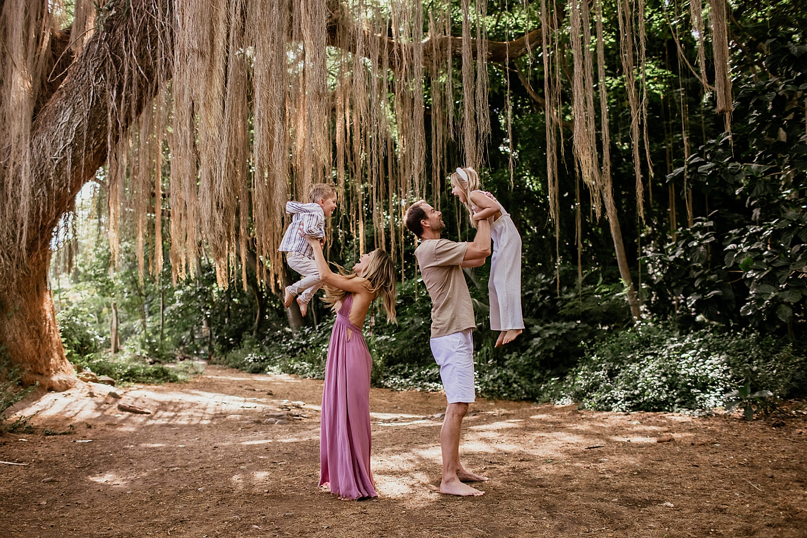 Parents holding up kids underneath a large tree with long dried leafs