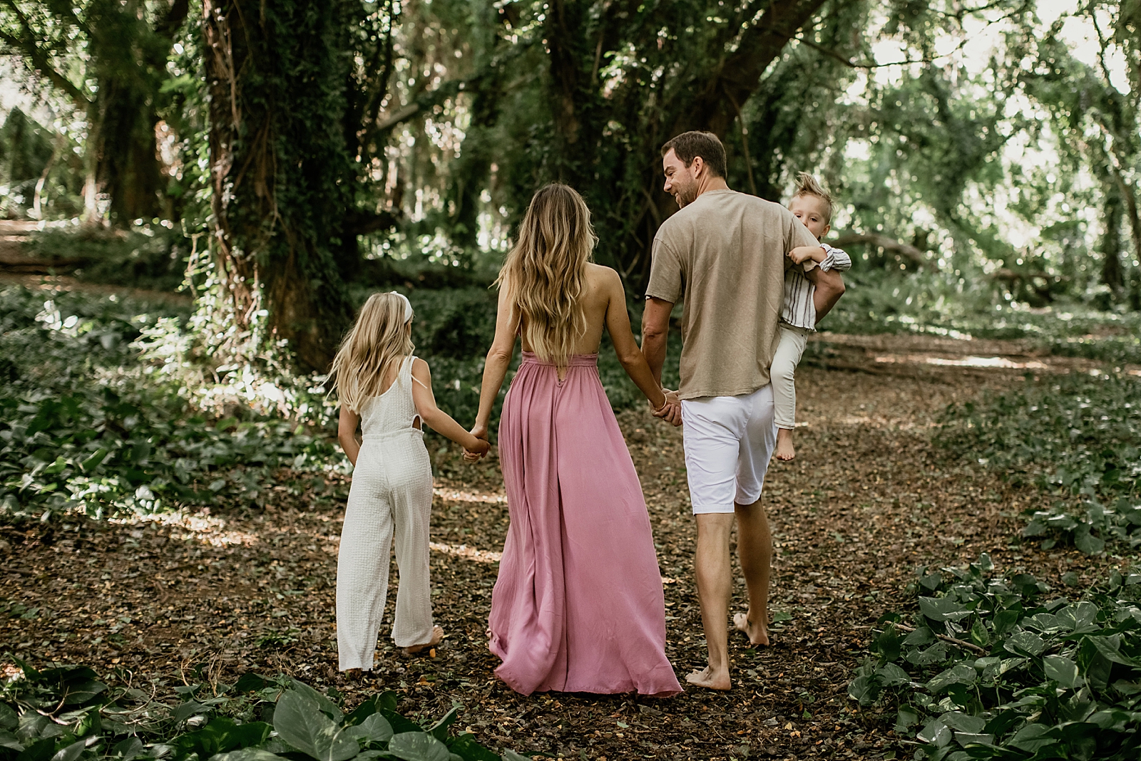 Back of family holding hands and Dad holding son and walking in green forest