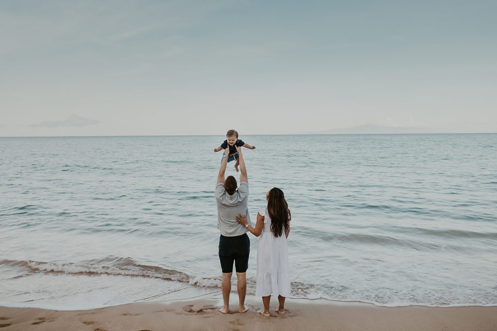 Father holding up son in the air by the ocean with Mother next to them